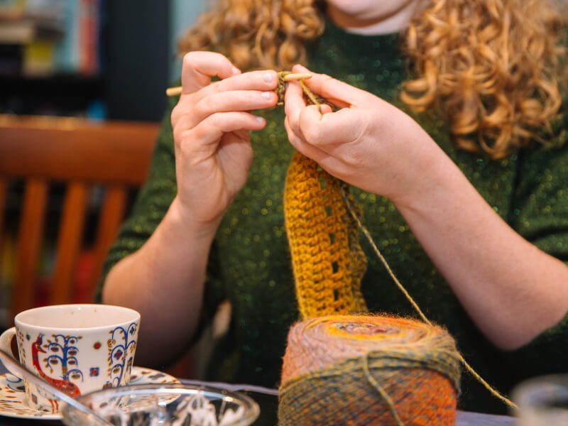 Woman crocheting with tea cup and yarn on table